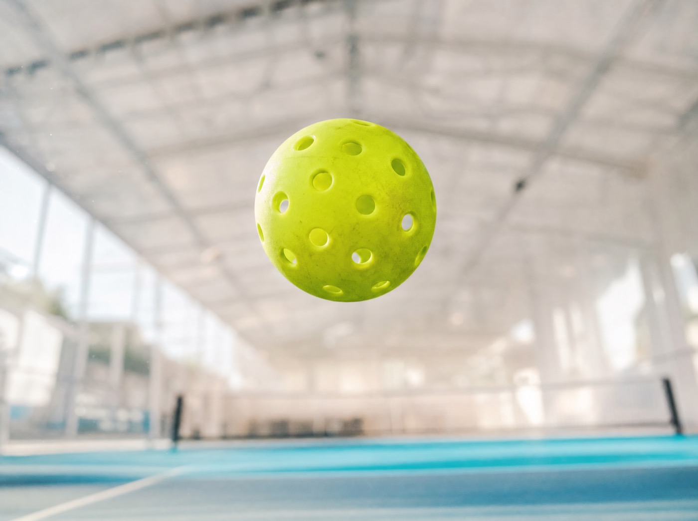 A pickleball mid-air in bright light.